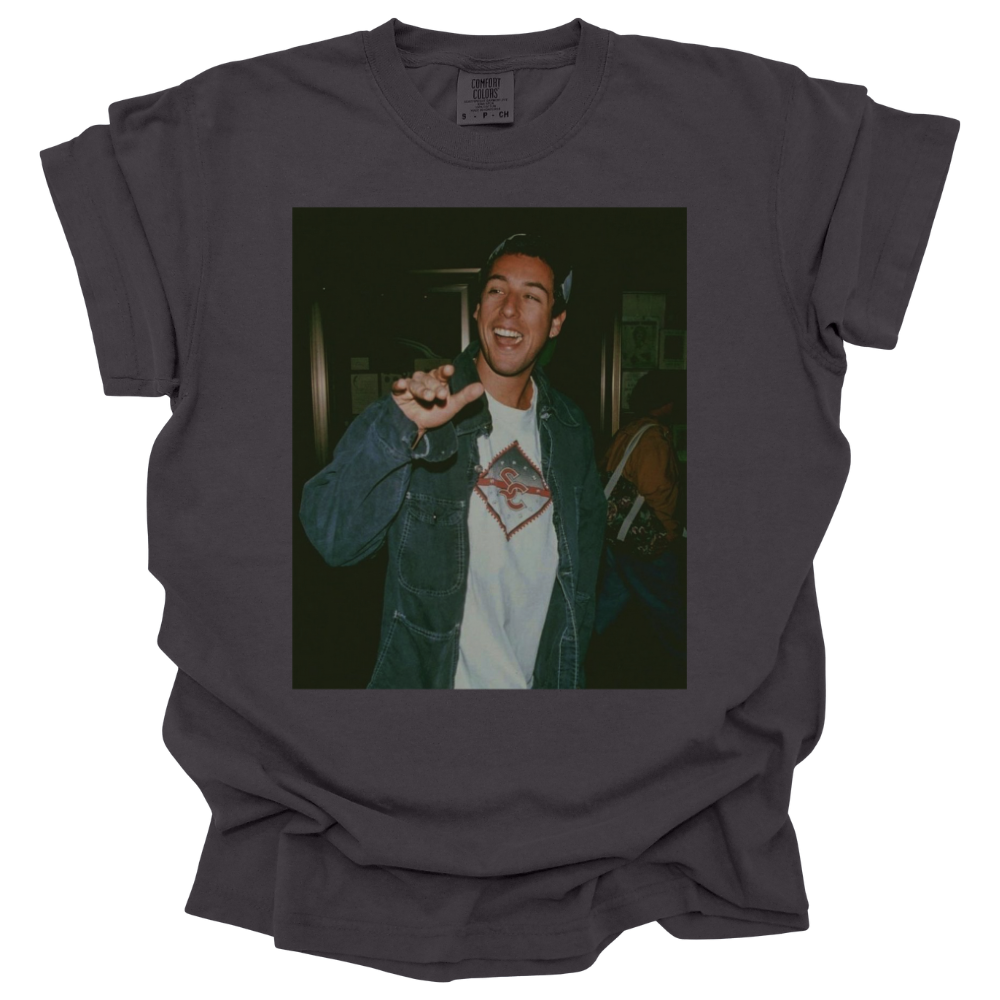 A pepper colored Comfort Colors T-shirt featuring a printed photograph of Adam Sandler waving. The vintage-style image has a nostalgic, laid-back feel, making it a statement piece for fans of classic '90s and 2000s pop culture