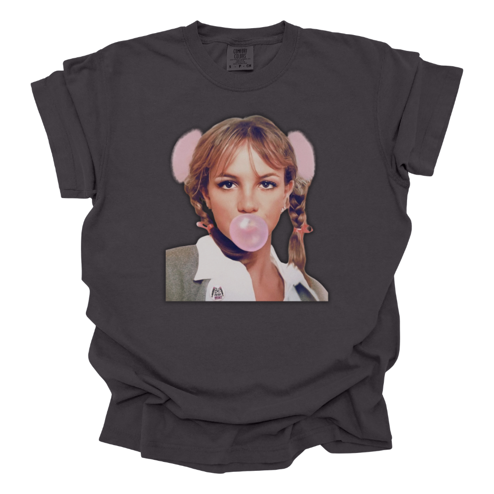 A dark graphite colored Comfort Colors T-shirt featuring an image of iconic Britney Spears from her ...Baby One More Time era, blowing a pink bubblegum bubble. She is dressed in her signature schoolgirl outfit with braided pigtails, a white collared shirt, and a gray cardigan. The design captures the ultimate late '90s and early 2000s pop nostalgia.