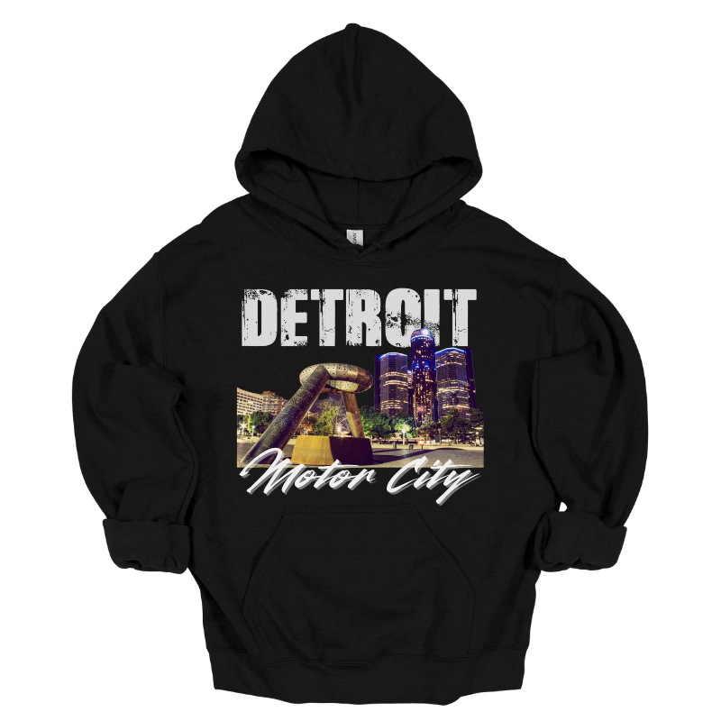 A black hoodie featuring a bold Detroit-themed graphic. The design showcases a nighttime view of the city's skyline with the iconic Joe Louis Fist monument in the foreground. 'DETROIT' is displayed in distressed white capital letters at the top, while 'Motor City' is written in a sleek cursive font below. The design captures the energy and pride of Detroit.