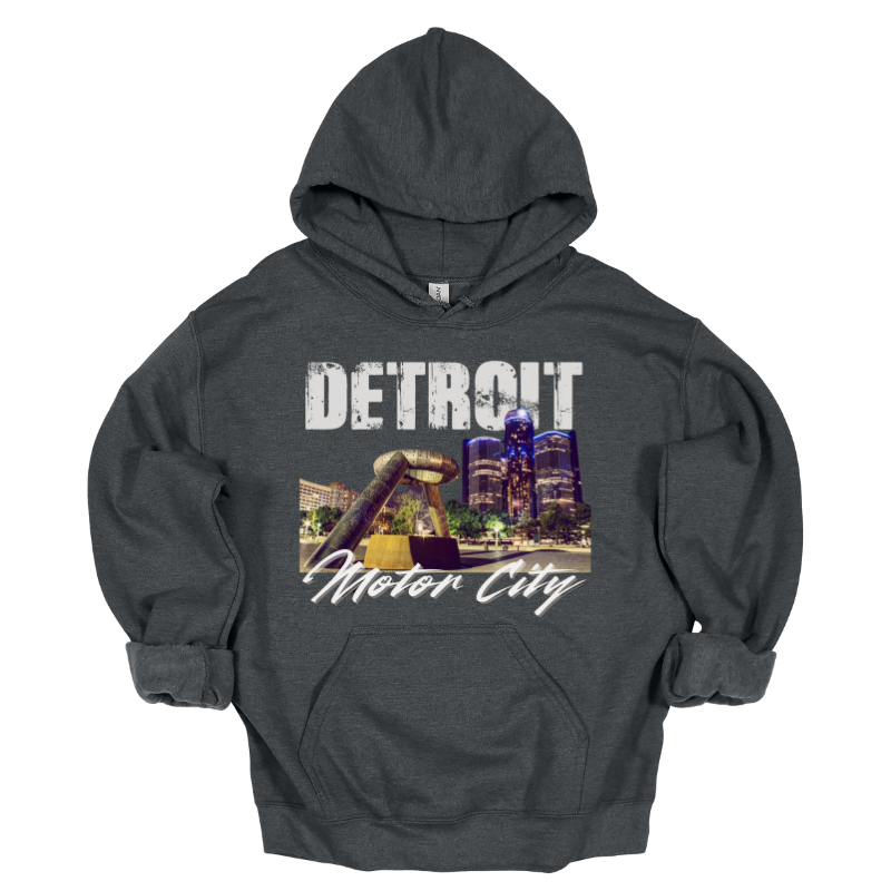 A gray hoodie featuring a bold Detroit-themed graphic. The design showcases a nighttime view of the city's skyline with the iconic Joe Louis Fist monument in the foreground. 'DETROIT' is displayed in distressed white capital letters at the top, while 'Motor City' is written in a sleek cursive font below. The design captures the energy and pride of Detroit.