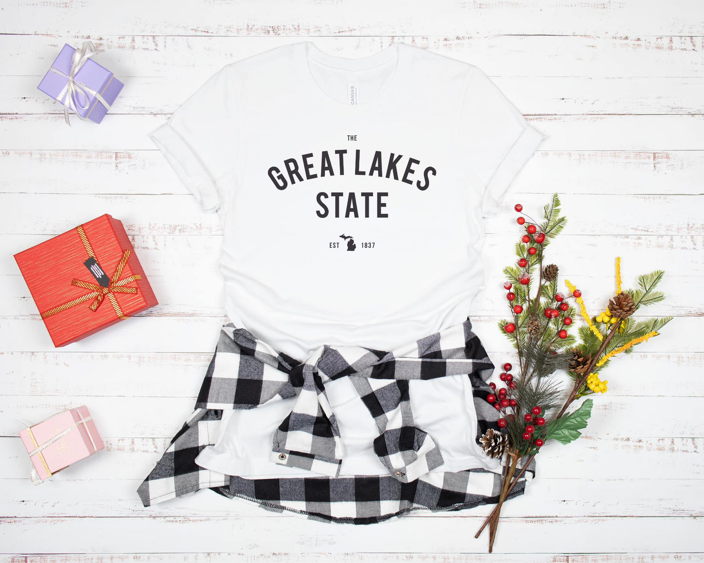 A classic white tee with 'The Great Lakes State' printed across the front in bold, arched lettering. Below, a small Michigan silhouette and 'EST. 1837' add a subtle state pride detail. The design has a timeless, minimal look, making it perfect for anyone who loves Michigan and the Great Lakes.