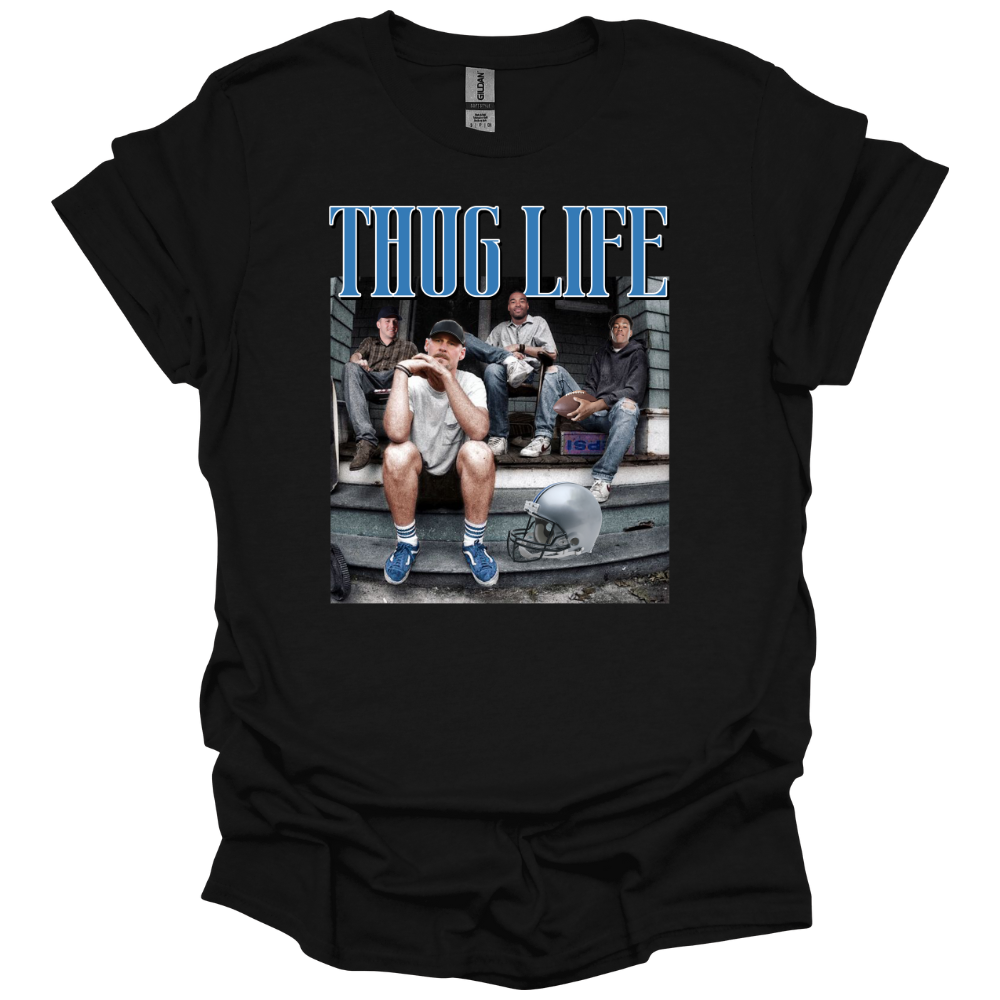 A black t-shirt sweatshirt featuring Detroit football figures Jared Goff, Calvin Johnson (Megatron), Dan Campbell, and Jahmyr Gibbs sitting on a porch. Jared Goff is in the foreground wearing a cap and blue sneakers, with a football helmet placed on the ground nearby. The words 'THUG LIFE' are printed in bold, blue Old English-style font above the image. The design has a humorous, nostalgic, and gritty vibe, perfect for Detroit football fans.