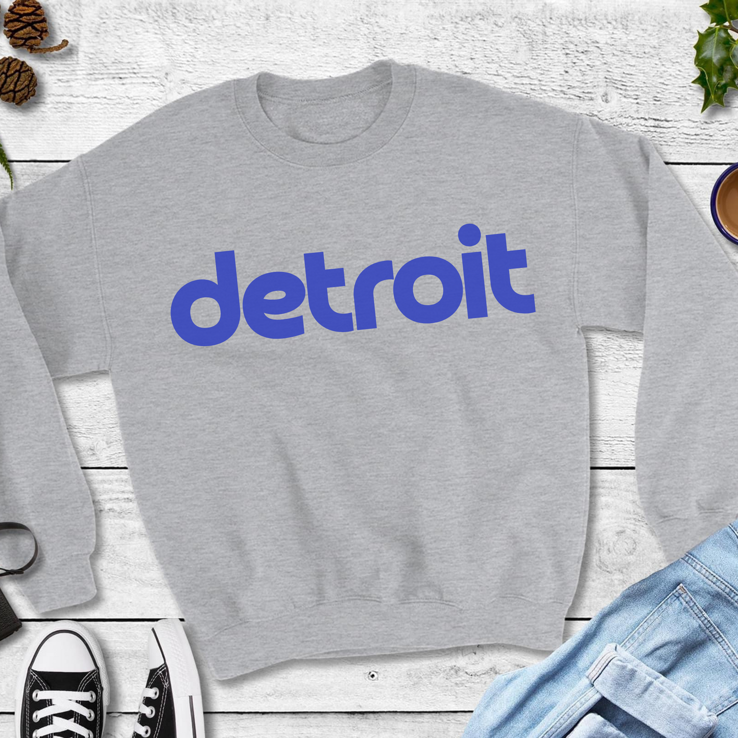 A heather gray Crewneck featuring the word 'detroit' in bold, modern blue lowercase lettering across the chest. The minimalist design gives a clean and stylish look, perfect for representing the Motor City in a simple yet bold way.
