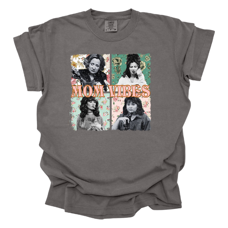 This Mom Vibes Tee is a pepper color T-shirt featuring tv mom icons Kitty Forman, Roseanne Connor, Sophia Petrillo, and Peggy Bundy each set against a retro floral background with old "mom vibes" text
