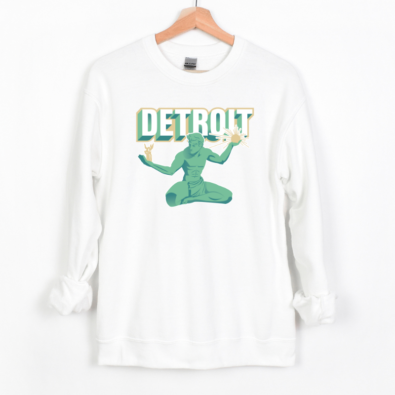 The Spirit of Detroit Crewneck is a white crewneck sweatshirt featuring a stylized illustration of the Spirit of Detroit statue in green and teal tones. The design includes bold, retro-style "DETROIT" text with a 3D effect, giving it a modern yet classic city pride look