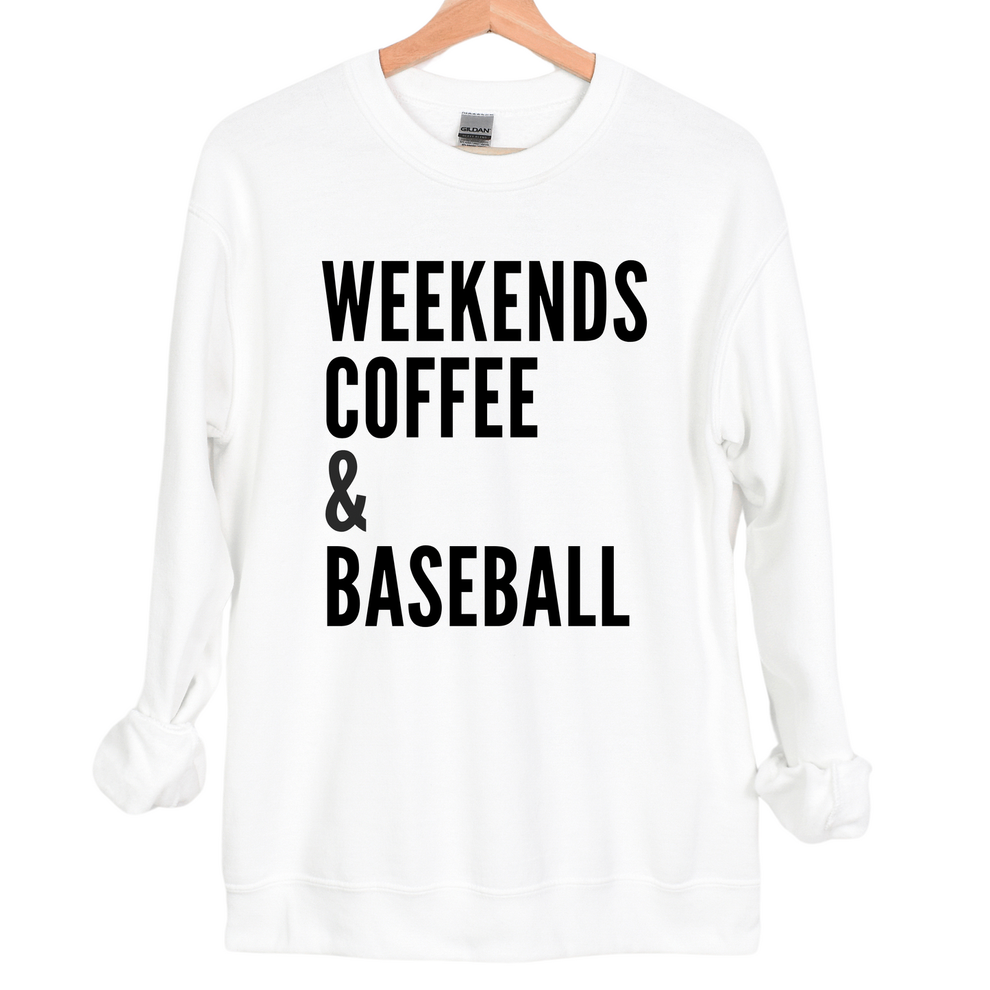 A white crewneck sweatshirt featuring bold black text that reads 'WEEKENDS, COFFEE & BASEBALL' stacked vertically in a simple, modern font. The cozy design is perfect for casual weekends and baseball lovers.