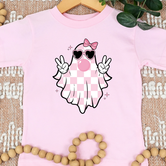 Toddler pink Halloween T-shirt with a checkered ghost wearing sunglasses, a bow, and blowing bubblegum while flashing peace signs.