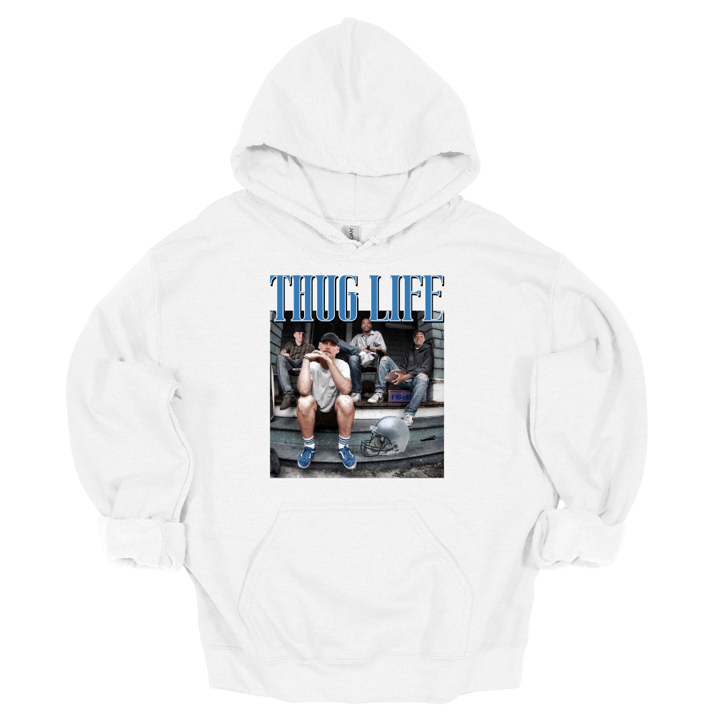A white hoodie sweatshirt featuring Detroit football figures Jared Goff, Calvin Johnson (Megatron), Dan Campbell, and Jahmyr Gibbs sitting on a porch. Jared Goff is in the foreground wearing a cap and blue sneakers, with a football helmet placed on the ground nearby. The words 'THUG LIFE' are printed in bold, blue Old English-style font above the image. The design has a humorous, nostalgic, and gritty vibe, perfect for Detroit football fans.