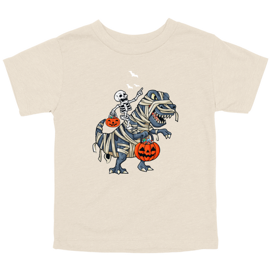 Cute Halloween graphic on natural colored toddler shirt with skeleton riding a mummy-wrapped T-Rex holding pumpkins